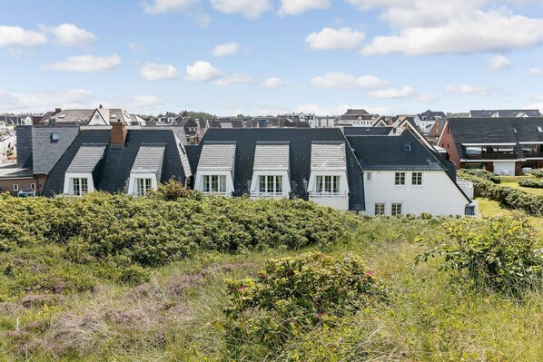 A row of houses with steeply pitched roofs, surrounded by dense shrubbery.