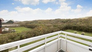 A deck with a white railing overlooking a landscaped garden and a hilly landscape.
