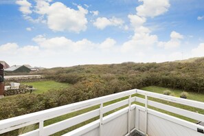 A deck with a white railing overlooking a landscaped garden and a hilly landscape.