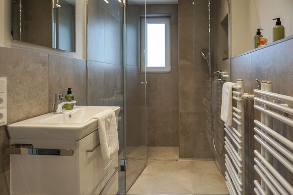 Une salle de bain moderne avec une douche à parois de verre, un lavabo avec une serviette et un porte-serviettes blanc.