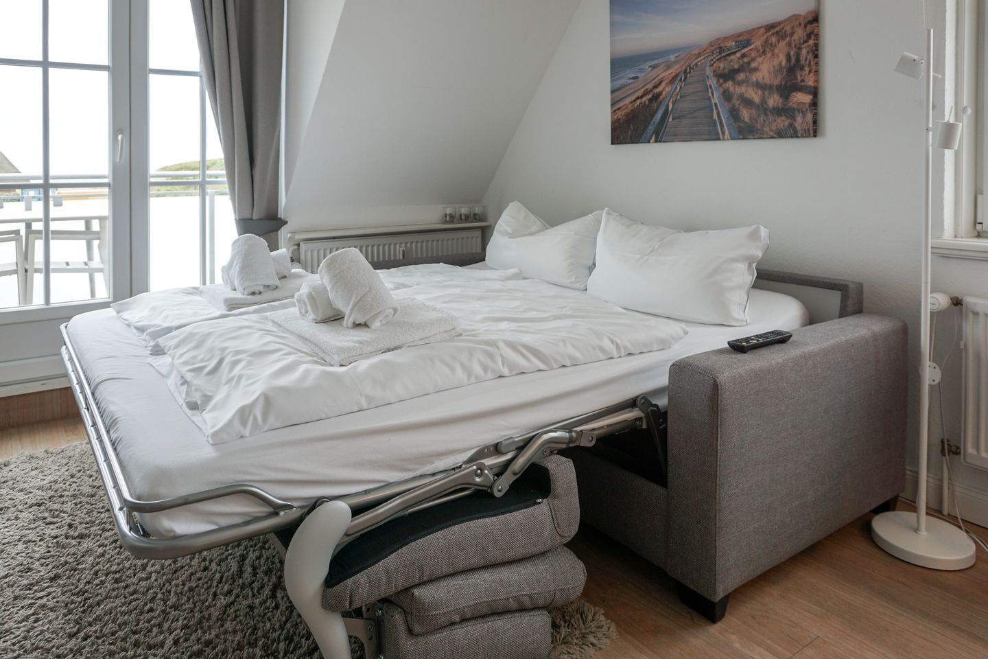 Une chambre moderne avec un lit convertible, une table de chevet, une lampe sur pied et une grande fenêtre donnant sur un beau paysage.