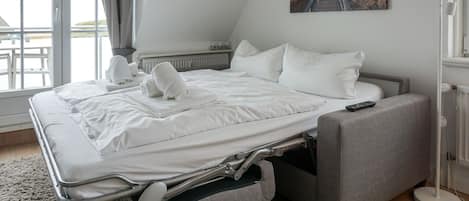 Une chambre moderne avec un lit convertible, une table de chevet, une lampe sur pied et une grande fenêtre donnant sur un beau paysage.