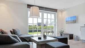 Una sala de estar moderna con un sofá, una mesa de centro, un reposapiés y un amplio ventanal con vistas al exterior.