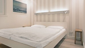 Un dormitorio con cama, mesita de noche, lámpara de pared y un cuadro.