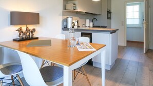 Une cuisine moderne avec une table en bois, des chaises blanches et un petit îlot central doté d’un évier.