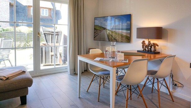Un espace repas moderne avec une table en bois, des chaises blanches et une grande fenêtre donnant sur un jardin.