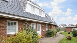 Une maison à deux étages, avec une façade en briques, des fenêtres blanches et un toit en pente.