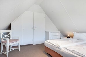 A bedroom with a sloped ceiling, a bed, a chair, a nightstand, and a wardrobe.
