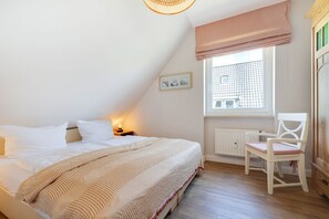Quarto com cama, cadeira, janela com vista e radiador.