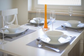 A dining table set with white plates, bowls, cutlery, and a tall orange vase.