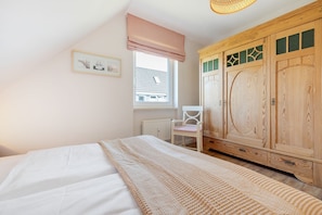 Un dormitorio con cama, armario de madera, ventana con vistas y una silla.