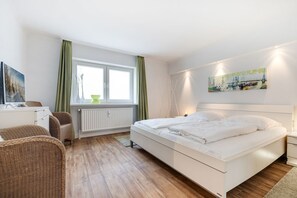 Een slaapkamer met een bed, een bureau, een stoel, een radiator en een raam met gordijnen.