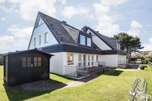 A two-story house with a sloped roof, a small attached garage, and a paved driveway leading to a gated entrance.