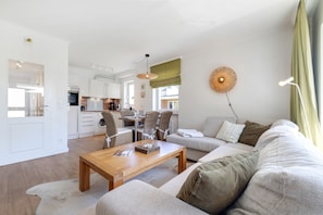 En moderne stue med sofa, sofabord i træ og spiseplads med stole og bord.