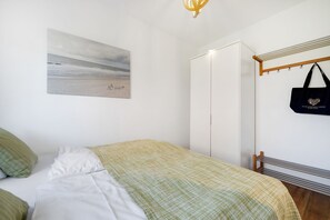 Une chambre à coucher avec un lit, une armoire, un sac suspendu et un tableau représentant une plage.