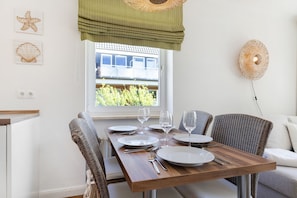 A dining area with a wooden table set for four, wicker chairs, a view of greenery outside, and a wicker wall decoration.