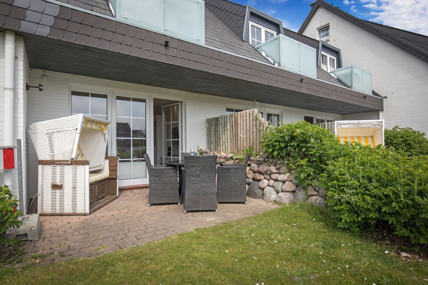 A modern house with a patio area featuring wicker furniture, a stone wall, and a small garden.