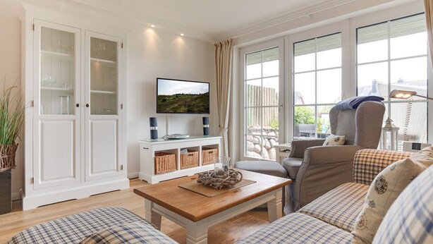 A living room with a television, a sofa set, a coffee table, and a cabinet with glass doors. - Landhaus Westerhörn, Sölring Tir, App. 1 - Beste Lage Zwischen Meer und Dorfteich. Sehr Schöne (Wenningstedt-Braderup (Sylt))