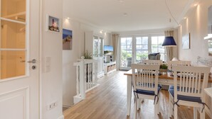 A spacious living area with a dining table, chairs, a TV, and a balcony with a view. - Landhaus Westerhörn, Sölring Tir, App. 1 - Beste Lage Zwischen Meer und Dorfteich. Sehr Schöne (Wenningstedt-Braderup (Sylt))