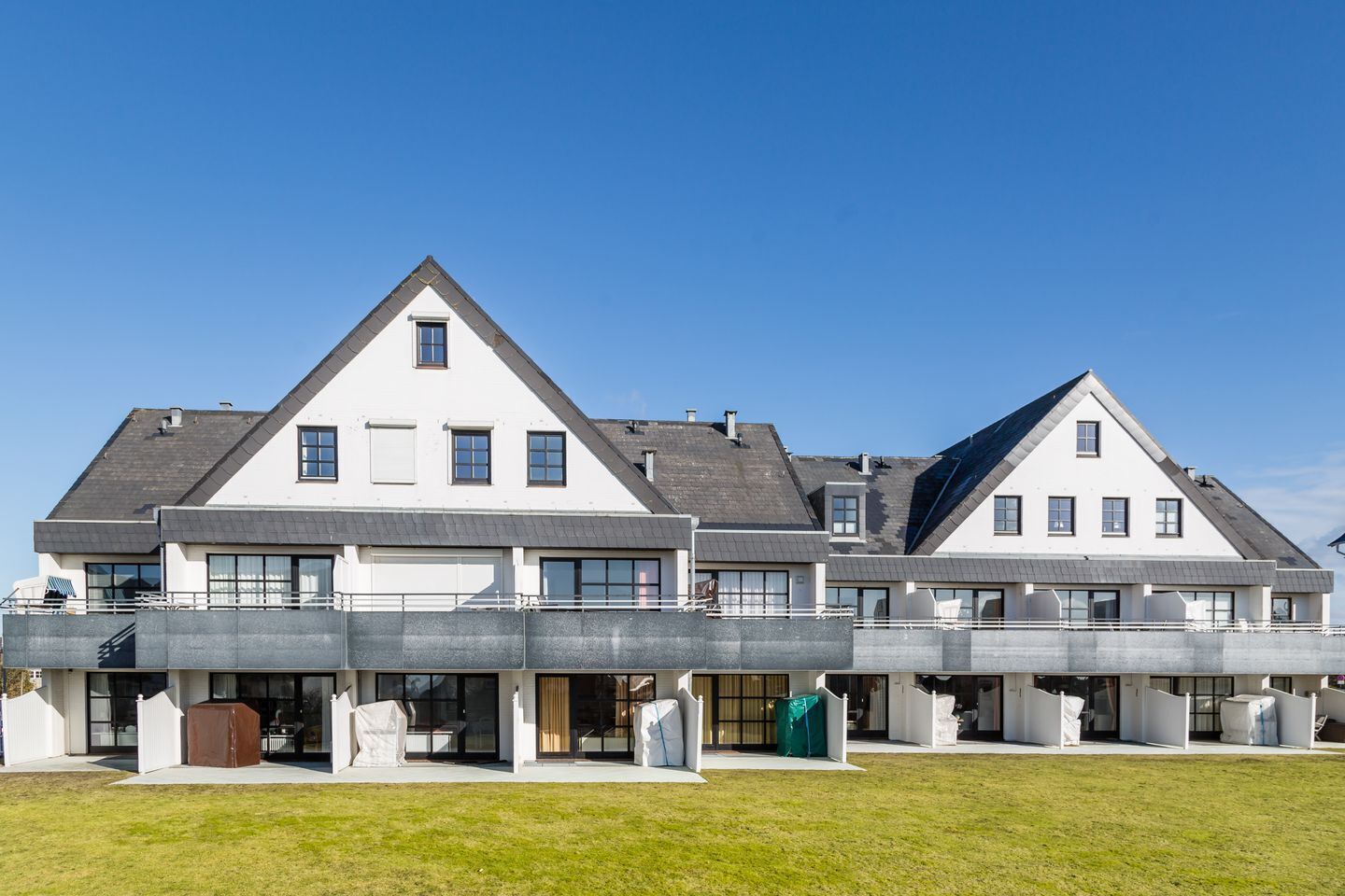 Een rij moderne twee-onder-een-doorwoningen met grote ramen en een plat dak.