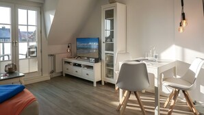 Une pièce moderne et bien éclairée, comprenant une table à manger, des chaises, un téléviseur et un meuble.