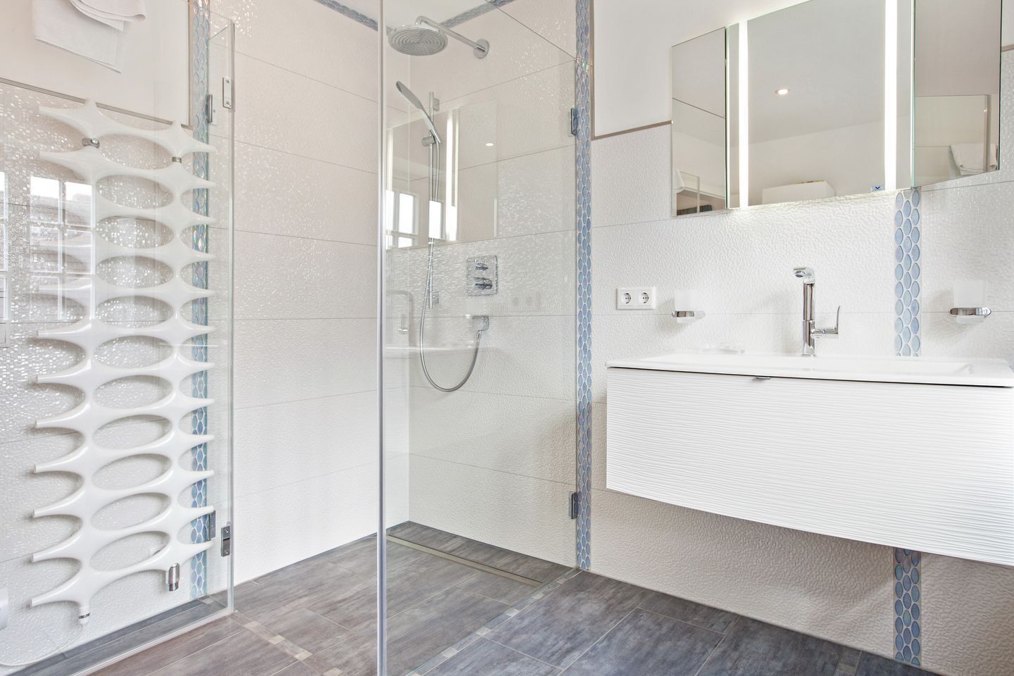 A modern bathroom with a glass shower enclosure, a white sink with a mirror, and a tiled floor.