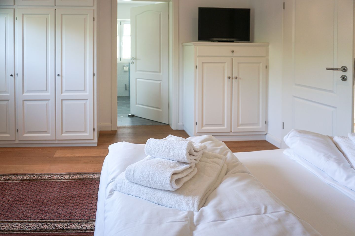 Una habitación de hotel con una cama, un armario blanco y un televisor encima del armario.