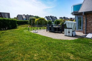 Un jardin à l’arrière d’une maison, avec une terrasse, du mobilier d’extérieur et une haie.