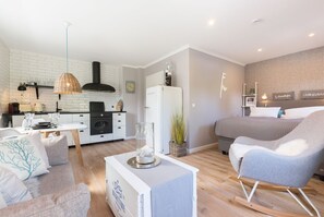 En moderne lejlighed med køkken, spiseområde og stue med en stor grå sofa og et lille hvidt bord.