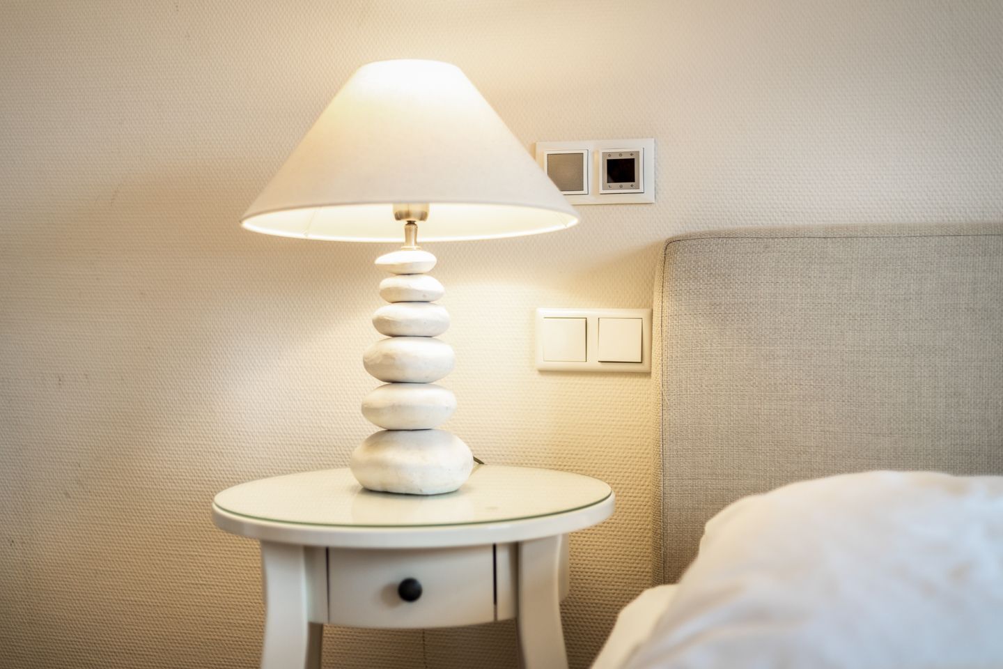 A bedside table with a lamp, a power outlet, and a light switch on the wall.