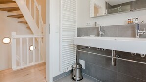 Ein modernes Badezimmer mit einem weißen Waschtisch, einem großen Spiegel und einer Duschkabine.