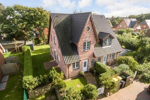 Une maison à deux étages, dotée d’un toit à forte pente, d’une façade en briques et d’un jardin bien entretenu.