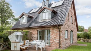 Ein zweistöckiges Haus mit Backsteinfassade, einem geneigten Dach und einer Terrasse mit Gartenmöbeln.