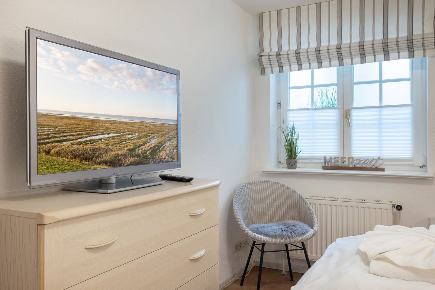 A bedroom with a TV on a dresser, a chair, a bed, and a window with blinds.