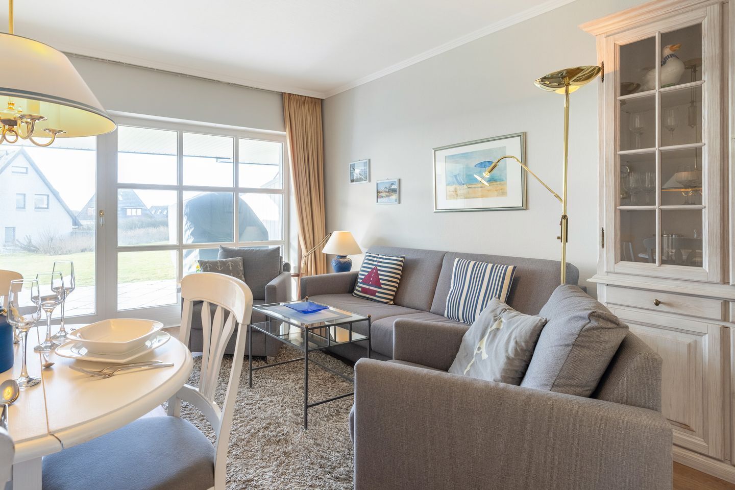 Ein Wohnzimmer mit einer Couch, Sesseln, einem Esstisch mit Gläsern und einem Schrank.
