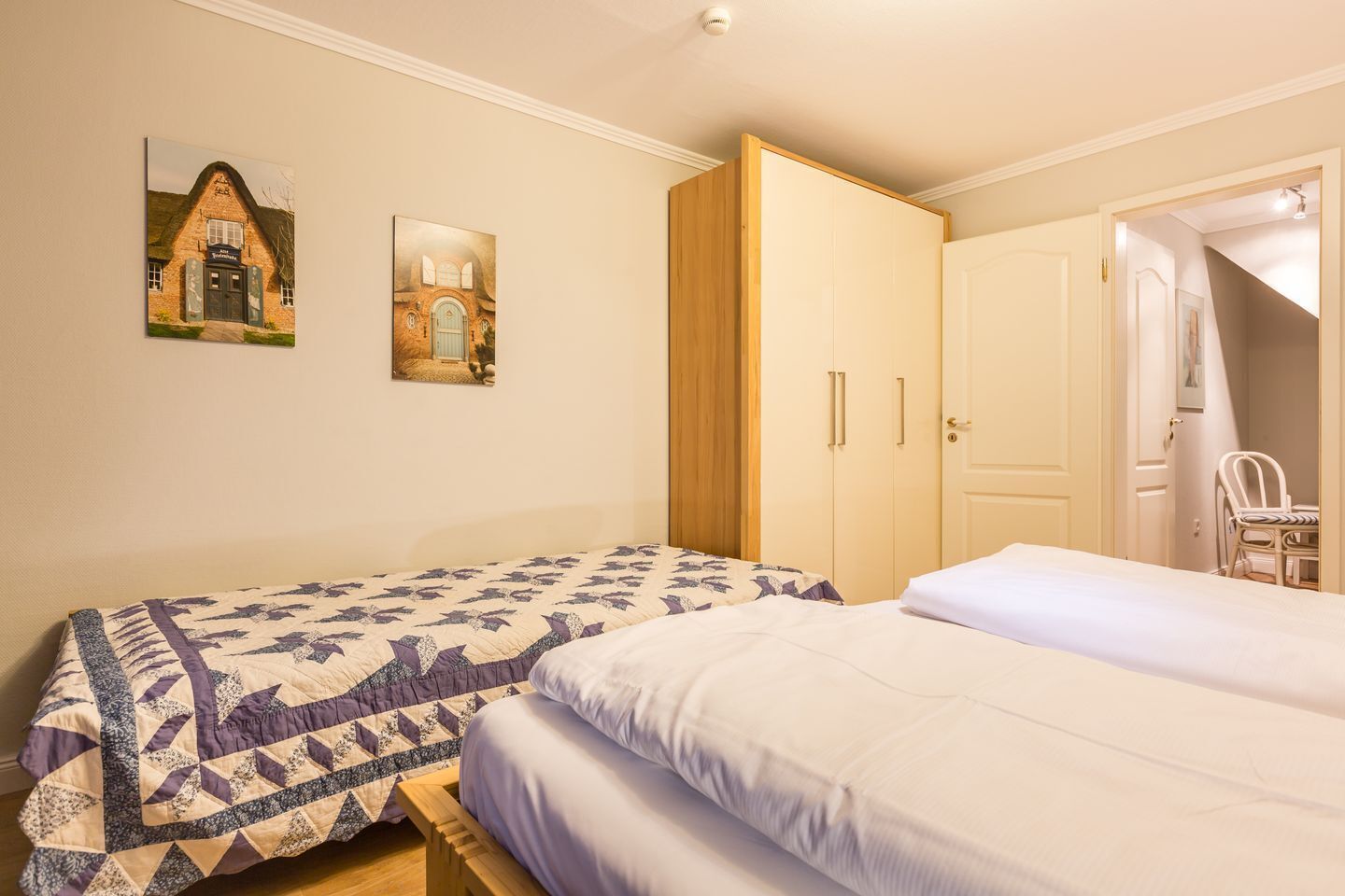 Un dormitorio con dos camas, un armario y dos cuadros colgados en la pared.