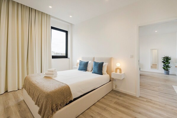 Une chambre à coucher moderne avec un grand lit, des lampes de chevet et une vue sur la ville par la fenêtre.