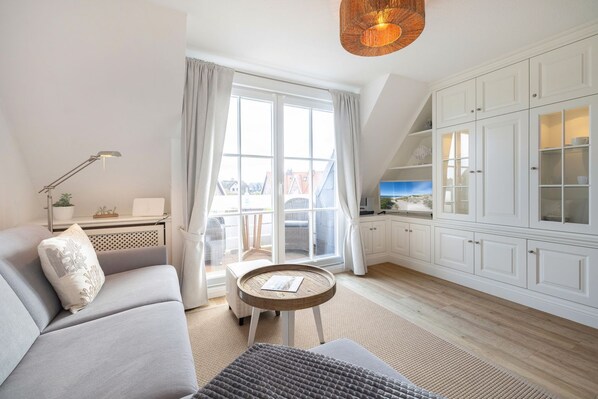 A modern living room with a sofa, a small round table, and a view of the city through large windows.