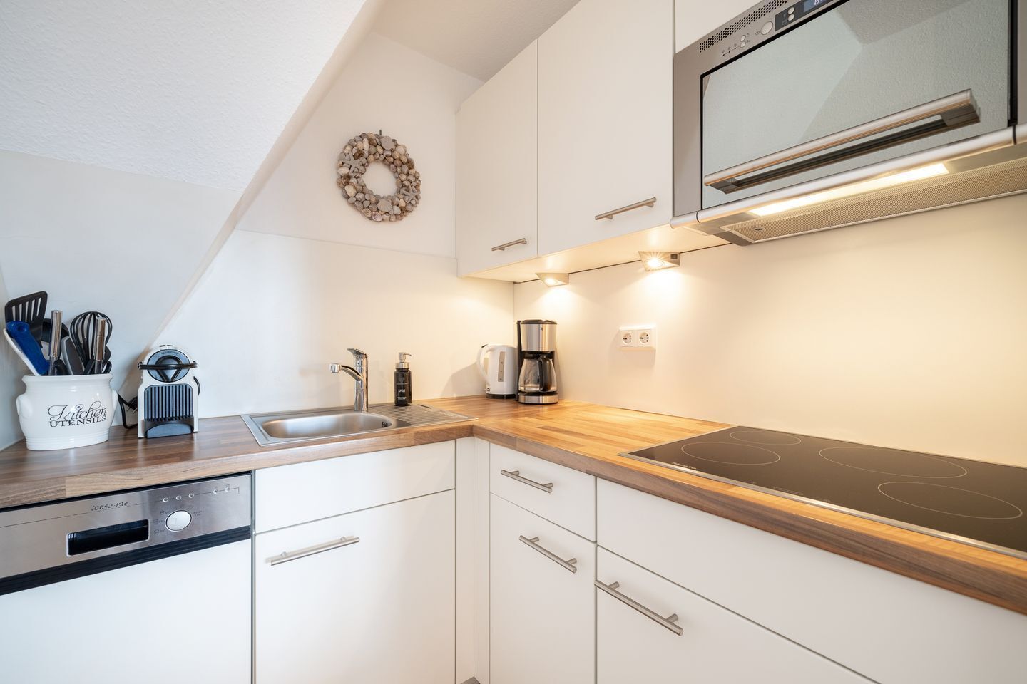 A modern kitchen with white cabinets, a stainless steel sink, a built-in oven, and a coffee maker.