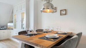 Ein Essbereich mit einem Holztisch, gedeckt für sechs Personen, weißen Schränken, einer Pendelleuchte und einem gerahmten Bild an der Wand.