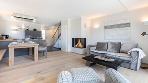 A modern living room with a fireplace, a sofa, a coffee table, and a dining area with a table and chairs.