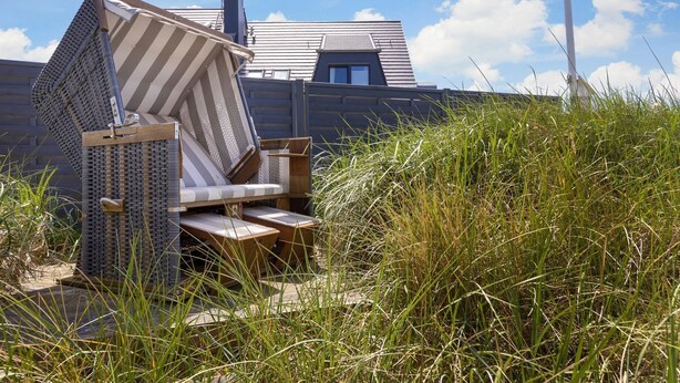 A beach chair in a grassy area with a house in the background.