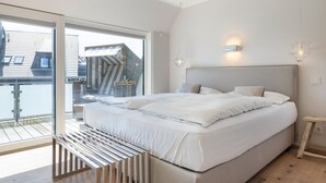 A modern bedroom with a large bed, a balcony, and a view of a building outside.