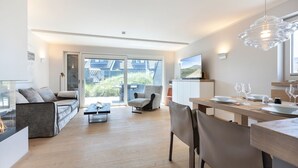 A modern living room with a sofa, a coffee table, and a dining area with chairs and a table set for a meal.