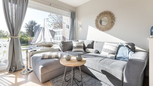 Ein modernes Wohnzimmer mit einem grauen Sofa, einem runden Holztisch und einem dekorativen Spiegel an der Wand.