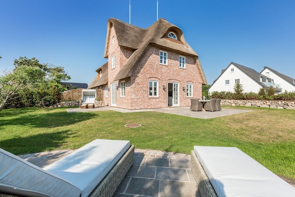 A house with a brick exterior and a thatched roof, a patio with outdoor furniture, and a well-maintained lawn.