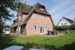 A brick house with a thatched roof, a patio with outdoor furniture, and a well-maintained lawn.