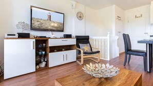 A modern living room with a flat-screen TV, a wooden coffee table, a white cabinet, and a black leather chair. - Sylter Refugium, App. 2 - Mitten im Beliebten Inselort Wenningstedt Befindet Sich Dieses Appartement (Wenningstedt-Braderup (Sylt))