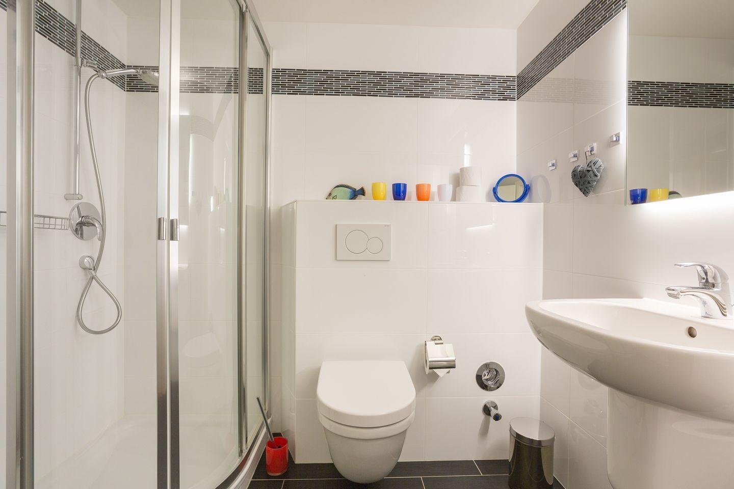 Et moderne badeværelse med en brusekabine i glas, et hvidt toilet og en vask med et spejl over.