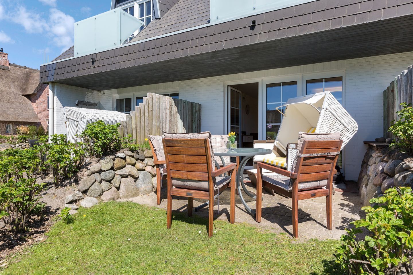 Een terras met een tafel en stoelen, een stenen muur en een huis met een schuin dak.